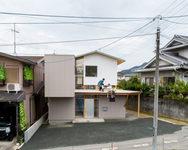 大きく張り出した庇は、きれいに手入れされた隣家の植栽とのつながりや平面的な広がりを考えて設置された。里道をはさんだ隣家の擁壁は2ｍの高さがあるため、まるで庇が隣家の地面につながっているように感じられる。同時に里道と敷地の、ゆるやかなつながりも実現している
