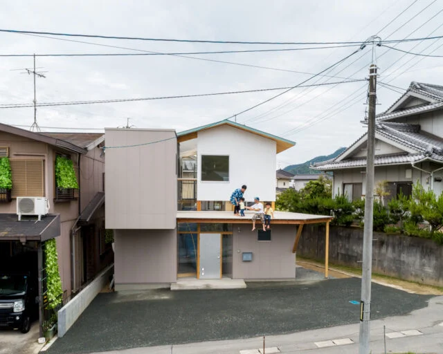 大きく張り出した庇は、きれいに手入れされた隣家の植栽とのつながりや平面的な広がりを考えて設置された。里道をはさんだ隣家の擁壁は2ｍの高さがあるため、まるで庇が隣家の地面につながっているように感じられる。同時に里道と敷地の、ゆるやかなつながりも実現している

