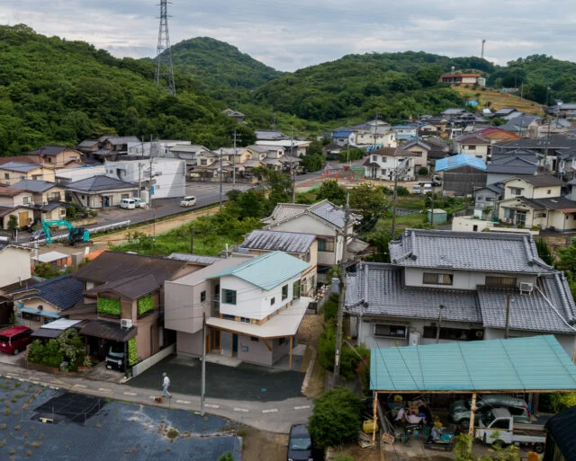 周辺環境。写真左側には比較的新しい家が並ぶ。家全体を2つにわけ、新しく建てられた周囲の家とボリュームが同じようになることを意識したのがよくわかる。切妻屋根は周囲に多く、色も周囲の家と近いものを使うなど、周囲に溶け込むプランとなっている
