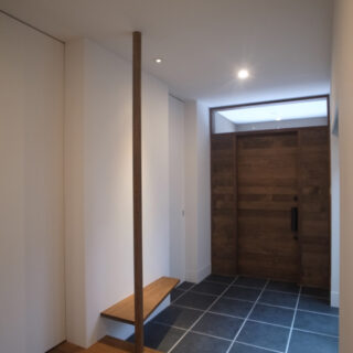 玄関扉は木板張りの特注製作です。 
造付けベンチと手摺を兼ねた柱がアクセントに。