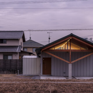 公園から見た夕景。公園側に窓はなく、完全に視線をカットしている。一方でハイサイドライトからは間接照明が照らす天井が見える。等間隔に設けられた梁と柱が美しい。軒が玄関側だけ長く出ているのは、玄関ドアや周辺が濡れないための工夫だ　

