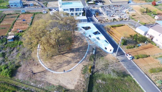 敷地全景（鳥瞰）。中央の円形の遊歩道に囲まれた部分が園庭。その右側の三角形の建物が今回の作品。部屋と廊下が蛇行して配置されていることがよくわかる。屋根がない部分が中庭で、その周囲をスロープの廊下で移動する