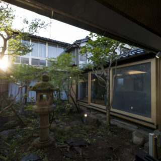 中庭と今回は未改修の町家（正面奥）。改修したリビングの窓（写真右）は、中庭がよく見えるように、幅1.8ｍの大きな引戸を設置した。窓枠はヒバ製で、庇の瓦との相性を考えて採用された
