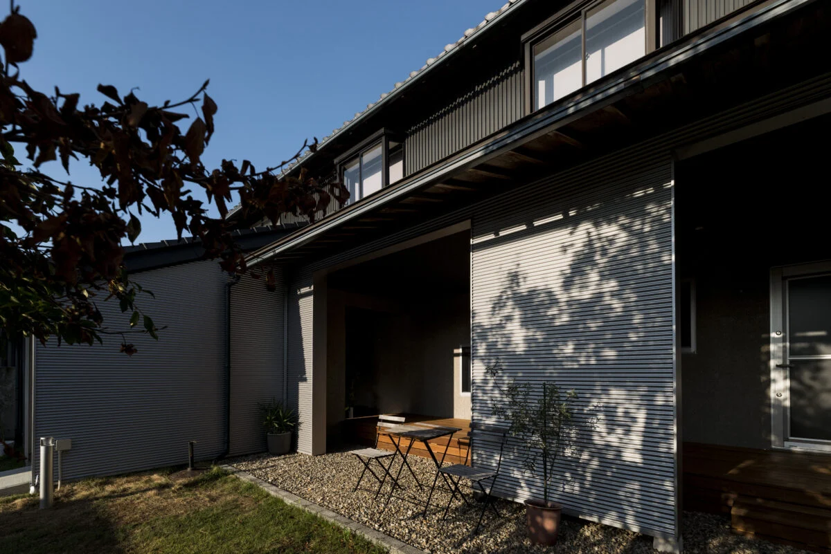 広い西側の庭から見たウッドデッキとピロティ（写真中央）。思い入れのある樹木が大きく生育し、美しい影を作る。後に増築されたエリアのため、2階部分は内外装ともに状態が良く、未改修だが違和感はない
