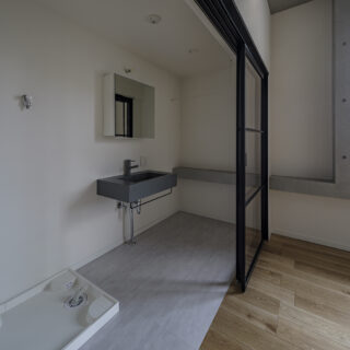 3階の北東角部屋、Ａタイプの水まわり。隣の寝室との仕切りは、圧迫感のないガラスの間仕切り。開け放しておけば空間を広々と使える。コンクリートの窓台は、寝室内の窓の下からそのまま洗面スペースへ。2つの空間がひと続きであることが感じられ、一体感が強調される
