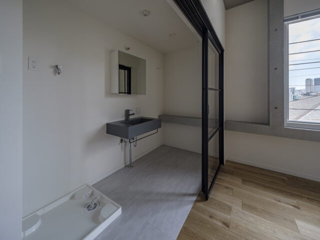 3階の北東角部屋、Ａタイプの水まわり。隣の寝室との仕切りは、圧迫感のないガラスの間仕切り。開け放しておけば空間を広々と使える。コンクリートの窓台は、寝室内の窓の下からそのまま洗面スペースへ。2つの空間がひと続きであることが感じられ、一体感が強調される
