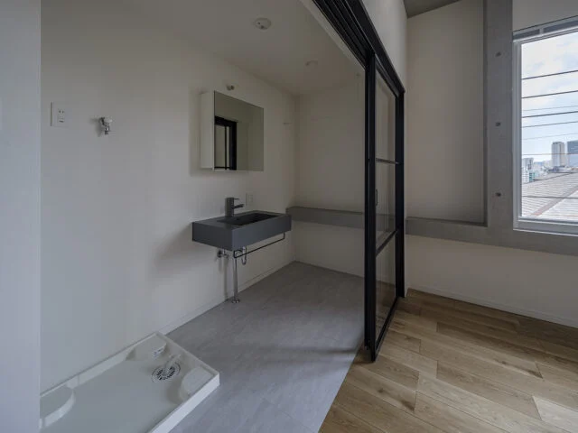 3階の北東角部屋、Ａタイプの水まわり。隣の寝室との仕切りは、圧迫感のないガラスの間仕切り。開け放しておけば空間を広々と使える。コンクリートの窓台は、寝室内の窓の下からそのまま洗面スペースへ。2つの空間がひと続きであることが感じられ、一体感が強調される
