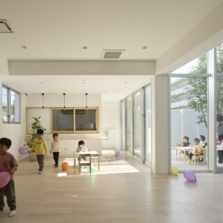 保育室から続くランチスペース。ガラス窓で仕切られた奥のスペースは厨房となっている。中庭と室内の床がフラットになっているので、小さな子どもでもつまづきにくく安心して出入りできる。季節や時間帯によっては、中庭に降り注ぐ陽光が室内にも届く