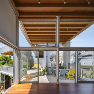 別角度のリビングから見た風景。奥にあるのが親世帯の棟で、その間をつなぐのが屋根付きテラス。左に奥庭の緑が見える。高い天井と全面ガラス、テラスの屋根が室内にまで続くことで、外と中の連続性を感じることができる