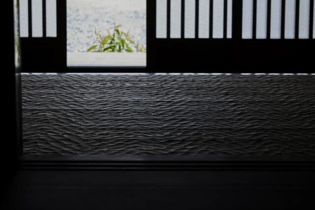 陰影の美しさは「窓辺の家」のテーマの1つ。玄関も日差しの入る明るい土間と薄暗い玄関ホールのコントラストが印象的。わずかな光で陰影が際立つ、なぐり加工の床も美しい