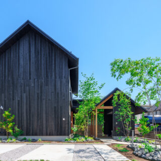 「双峰のいえ」の名のとおり大小２つの山が連なる。黒杉板の外観、ミカンやアオダモなどの木々が植えられた長いアプローチは、旅館か和食店を想像させる。