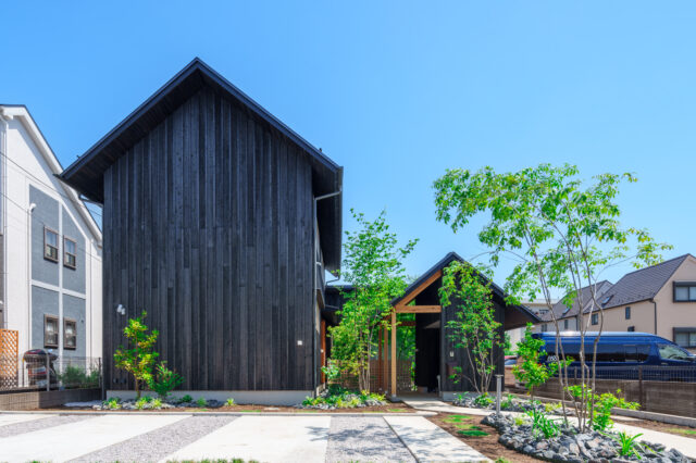 「双峰のいえ」の名のとおり大小２つの山が連なる。黒杉板の外観、ミカンやアオダモなどの木々が植えられた長いアプローチは、旅館か和食店を想像させる。