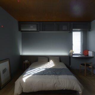 寝室。入眠効果を高めるため、暗めの配色で落ち着いた空間となっている。枕元には造作ボードを配し、こちらにも間接照明が組み込まれている
