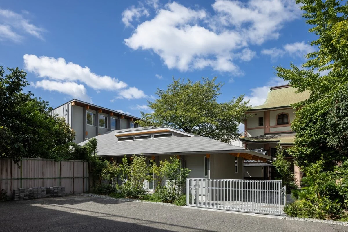 親世帯の外観。ライトグレーと木を合わせたモダンなデザインながら、軒の深い大きな屋根が落ち着いた雰囲気も漂わせている。写真右奥のお寺とも調和する、バランスの良い佇まい