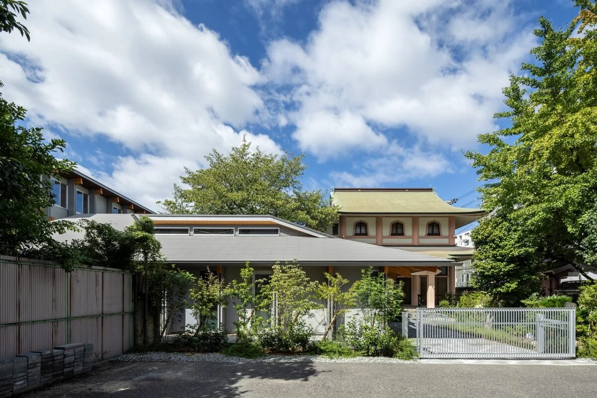親世帯（写真手前）はお寺（写真奥）と近いため、和の建築とのバランスを考慮して外観をデザイン。外壁はモダンな色使いだが、ゆったりとした大きな屋根と深い軒がお寺の軒と調和し、2つの建物が見事に馴染んでいる