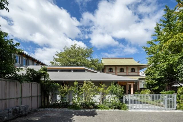 親世帯（写真手前）はお寺（写真奥）と近いため、和の建築とのバランスを考慮して外観をデザイン。外壁はモダンな色使いだが、ゆったりとした大きな屋根と深い軒がお寺の軒と調和し、2つの建物が見事に馴染んでいる