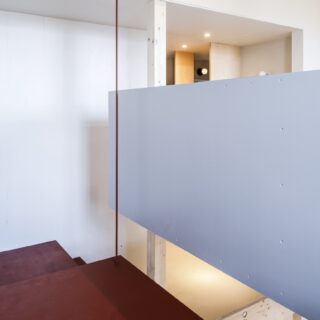 この階段の写真右が主寝室。2階も最小限の間仕切りでコストを圧縮。主寝室も壁で完全に囲っていない。階段沿いにハンガーパイプを設置してカーテンで仕切り、クロークとしても活用中