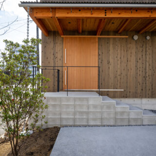 玄関は、コンクリート階段を上った先に。階段部分は建物本体と切り離すことで熱効率やシロアリ対策となるほか、異空間へ飛び込むイメージも。軒を深くとることで建物の構造面の補強にも。
photo：YASUO HAGIWARA