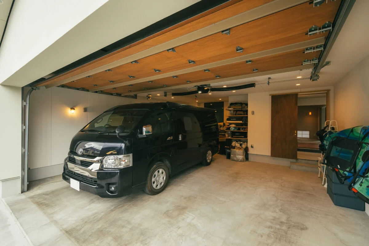 木製シャッター付きの屋内ガレージ。土間スペースに直接行くことができる（右）。キャンピングカーやキャンプ用品も収納でき、お施主様の趣味の部屋（左）からガラス越しに車を見ることもできる