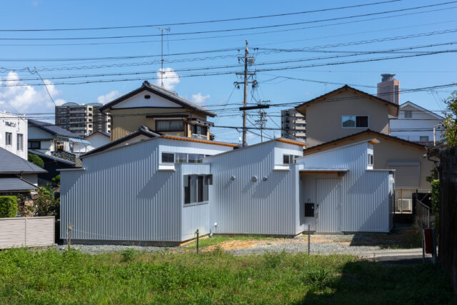道路側から見た外観。大中小の片流れ屋根が連なる、個性的なフォルム。接道する西面には一切窓を設けずにプライバシーを確保した。基本的にはコンクリート基礎だが、庭と接する箇所などはブロック基礎を採用。拡張や分離など、将来のリノベーションに向けて可能性を広げた