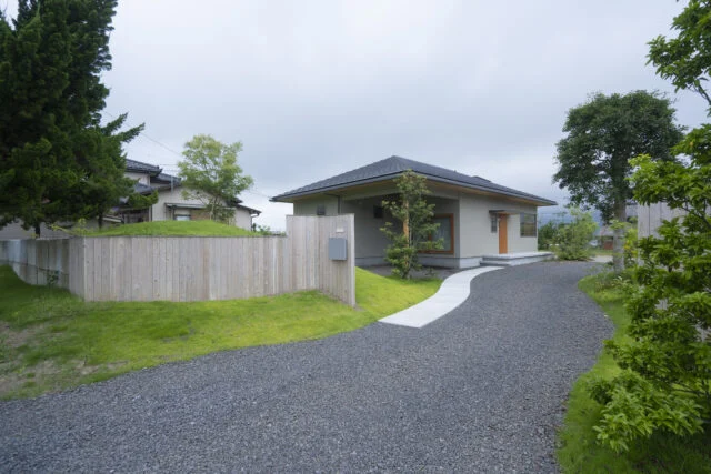 道路側から見た外観。建物の一角を屋根付きのテラスのような、用途を決めない空間として計画した。大きな洗濯物干しなど、便利使用されている。小高い丘の途中に外構が埋まっているよう。見た目も楽しい丘は高さ1.5ｍ程度あり、目隠しとしての役目を果たしている