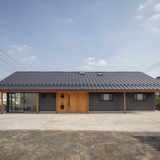 北の外観。手前のコンクリート広場は親族が集まる屋外の社交場。矢島さんがデザインした木製の玄関ドアは周囲の壁も板張りにして仕上げ、ガルバリウムの外壁とのバランスを取った。軒の木柱もアクセントとして生きていて、新年の門松なども似合う和モダンな佇まいになっている