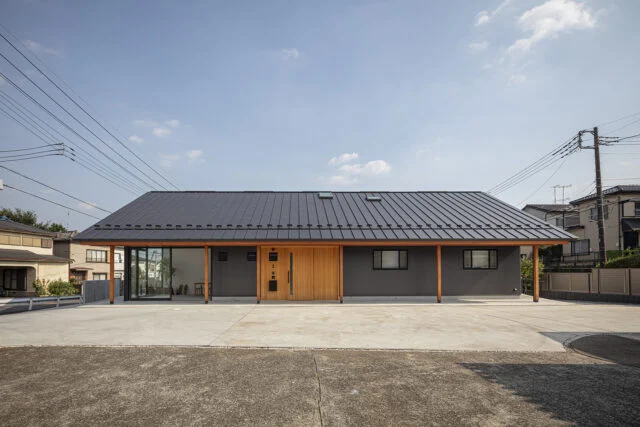 北の外観。手前のコンクリート広場は親族が集まる屋外の社交場。矢島さんがデザインした木製の玄関ドアは周囲の壁も板張りにして仕上げ、ガルバリウムの外壁とのバランスを取った。軒の木柱もアクセントとして生きていて、新年の門松なども似合う和モダンな佇まいになっている