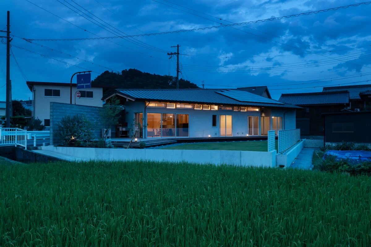 庭側外観夕景。室内から漏れ出る光が美しい。夜間でも境界壁のおかげで、外部からの視線を気にせず過ごすことができる。蛍の季節には、窓から庭の木にいる蛍を眺められるそうだ。妻は「毎年、とても神秘的で贅沢な時間を感じることができて満足です」と語ってくれた