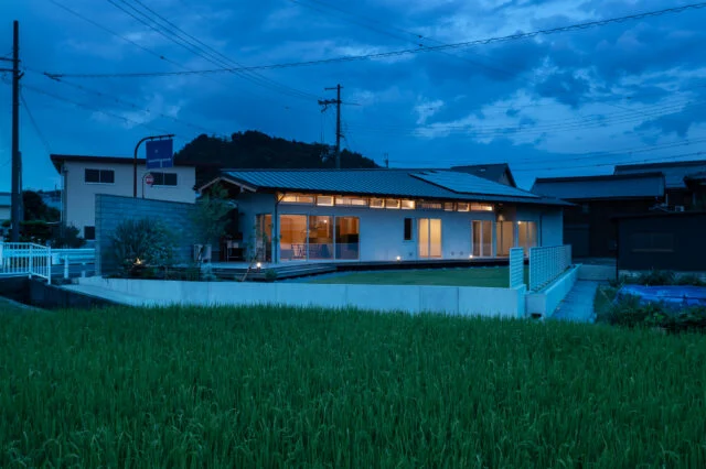 庭側外観夕景。室内から漏れ出る光が美しい。夜間でも境界壁のおかげで、外部からの視線を気にせず過ごすことができる。蛍の季節には、窓から庭の木にいる蛍を眺められるそうだ。妻は「毎年、とても神秘的で贅沢な時間を感じることができて満足です」と語ってくれた