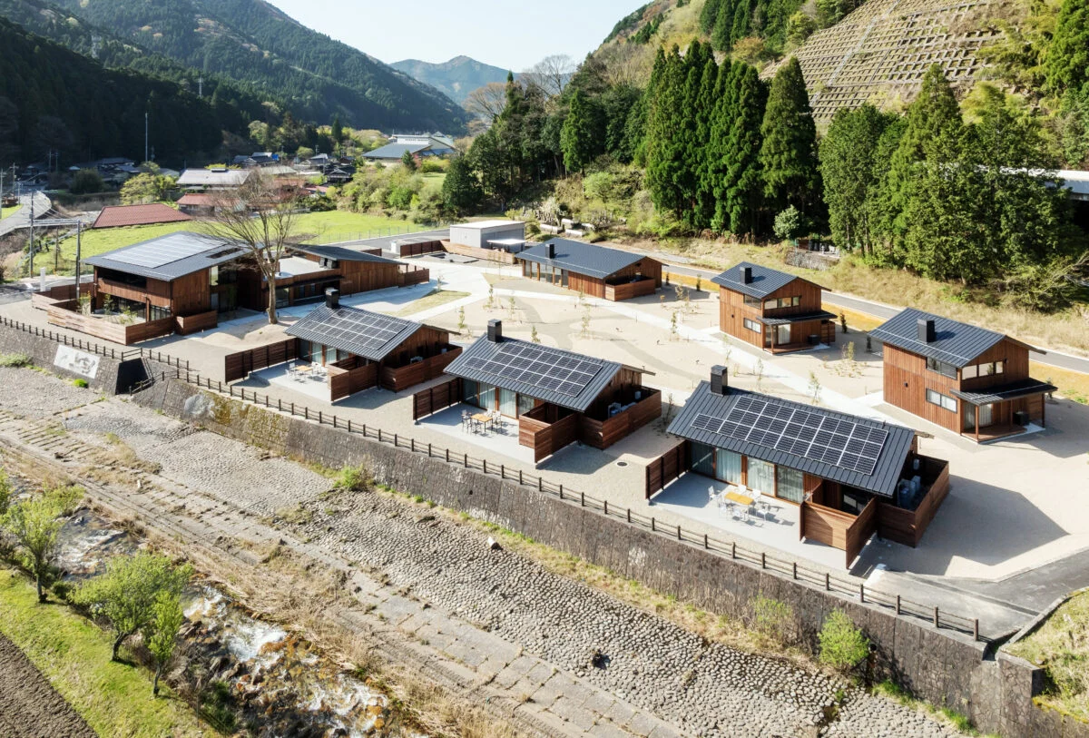 北側高所から見た全景。手前3棟並ぶのはA棟。下を流れる川の向こうには山がそびえている。川が流れ、さらに南からの光を受け止めた山の木々が美しいことから、リビングからテラスまでを一体化させて外に出やすくし、存分に楽しめるように整えた