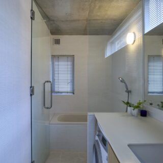 子世帯の水まわり。浴室、洗面、トイレを1カ所にまとめ、壁はモザイクタイルで統一。素材をそろえると全体が1つの空間として広く見える。内装カラーも、反射光の明るさで空間が広く見えることを狙って白をセレクト。浴室の仕切りはガラス戸にするなど、広く感じられる工夫が満載
