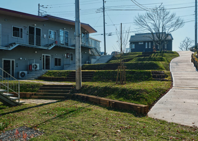 斜面はもともとの地形を生かし、ひな壇状に整地。平らにならすよりも土の掘削量が少なくて済むというメリットもある。写真左の山棟も、傾斜のある地形に素直に従ったデザイン。屋根や通路が山脈のようなラインを描いているのが面白い