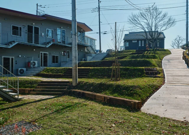 斜面はもともとの地形を生かし、ひな壇状に整地。平らにならすよりも土の掘削量が少なくて済むというメリットもある。写真左の山棟も、傾斜のある地形に素直に従ったデザイン。屋根や通路が山脈のようなラインを描いているのが面白い