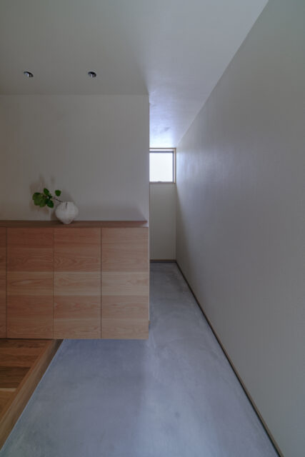 玄関土間。窓から入る光で漆喰壁の質感が際立つ。奥はキャンプ用品などをしまえる土間収納