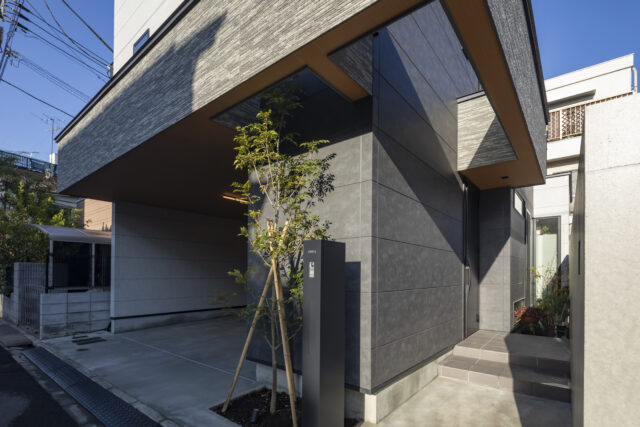 外観。画像右は玄関ポーチ、奥にお母さまが植栽を楽しむ坪庭がある。左のガレージからも直接室内に入れるよう計画した。ガレージ脇、玄関扉から手前はシューズインクローゼット。収納力は抜群で、2世帯分の納戸としても使われている