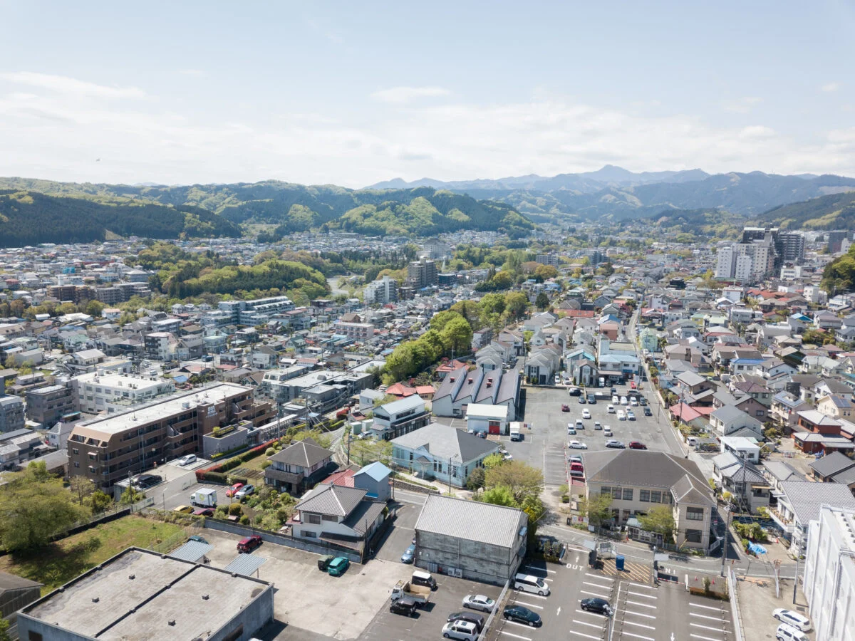 青梅の街並み。写真中央のパステルブルーの建物が、都立繊維試験場だったシネマネコ。敷地周囲には、倉庫をリノベーションしたダイニング＆ギャラリー、旧織物加工工場のさくらファクトリー工房、100名収容可能なホールを持つ協同組合本館があり、４棟が国登録有形文化財に指定されている。