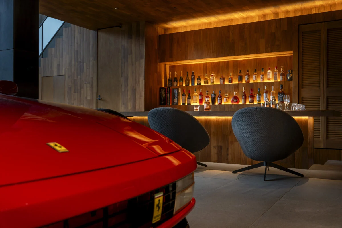 ギャラリーの一角にあるバーコーナー。コレクションカーを間近に眺めてお酒を楽しむ至福の時間は、クライアントへの最高のおもてなし。バーは店舗設計の知見を生かしてボトルが引き立つ照明付きの棚や、手元が見えないすっきりとしたカウンターをデザインしている