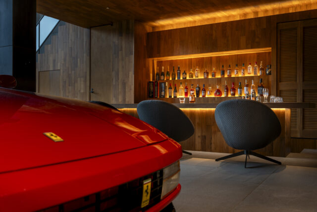 ギャラリーの一角にあるバーコーナー。コレクションカーを間近に眺めてお酒を楽しむ至福の時間は、クライアントへの最高のおもてなし。バーは店舗設計の知見を生かしてボトルが引き立つ照明付きの棚や、手元が見えないすっきりとしたカウンターをデザインしている