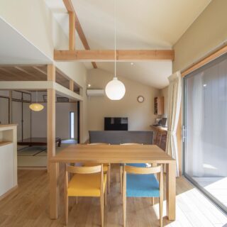 親世帯のダイニング。構造材を表しにすることで、木の家をという要望に応えた。家具も高杉さんがセレクト。大きな窓から自然豊かな庭が見える。キッチン（写真左）には造作カウンターを配置。収納と手元を隠す機能を併せ持つ