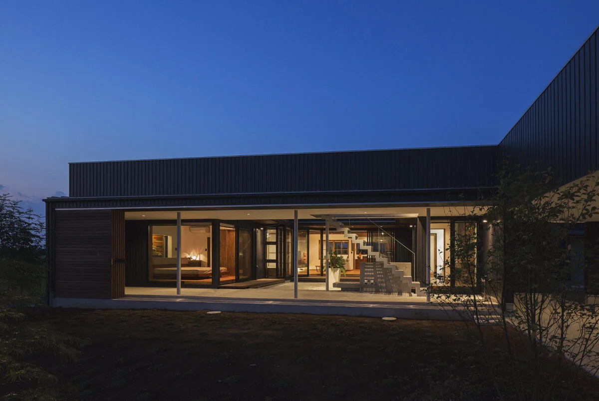 南の外観の夕景。建物と中庭はピロティ＋建具によって守られているため、中庭に面した住空間は大胆なガラス張り。日が落ちて明かりがともると建物そのものがガラス箱の照明のように光り輝き、高級レストランやホテルのような非日常感が漂う