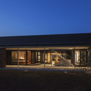 南の外観の夕景。建物と中庭はピロティ＋建具によって守られているため、中庭に面した住空間は大胆なガラス張り。日が落ちて明かりがともると建物そのものがガラス箱の照明のように光り輝き、高級レストランやホテルのような非日常感が漂う
