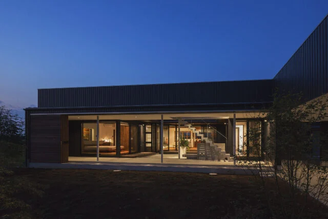 南の外観の夕景。建物と中庭はピロティ＋建具によって守られているため、中庭に面した住空間は大胆なガラス張り。日が落ちて明かりがともると建物そのものがガラス箱の照明のように光り輝き、高級レストランやホテルのような非日常感が漂う
