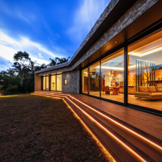 お施主さまの生活する「RETREAT HOME」。画像奥、折れ曲がった先がゲストエリア、手前がプライベート空間。室内にははっきりとした区切りをつくり、庭側は長いデッキで一続きとした。デッキの階段にはライン照明を入れ、贅沢な長さを強調