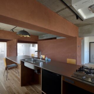キッチンから家を見渡す。画像右、エントランスから居住空間に入る部分の仕切りだけは、暑さ寒さ対策として閉じられることが多いとのこと。室内に行き止まりがなく、見通せるおかげでお子さまの居場所や様子がわかり、安心感がある。印象的なランプシェードは川井さんの自作