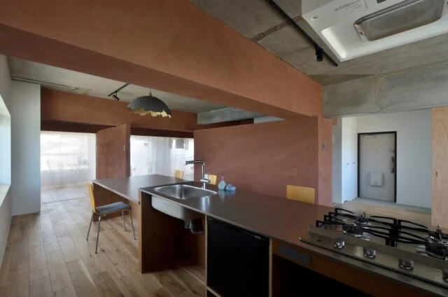 キッチンから家を見渡す。画像右、エントランスから居住空間に入る部分の仕切りだけは、暑さ寒さ対策として閉じられることが多いとのこと。室内に行き止まりがなく、見通せるおかげでお子さまの居場所や様子がわかり、安心感がある。印象的なランプシェードは川井さんの自作
