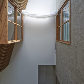 洋室に窓を設けることで、廊下から見るとまるで2軒の家が隣り合っているような風景に。向かって左側の杉板の壁を天窓側に傾け、天窓から入る日射量をコントロールしている。
