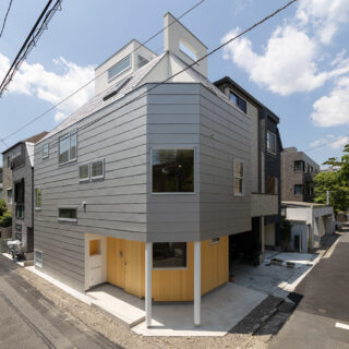 北東側から見た外観。コンパクトながら角地でよい立地だと2人。道路の向かいは学校であり、人通りは多いが視界や眺望は確保しやすい。外壁は主にガルバリウム鋼板を採用。歩行者の目に入りやすい１階の外壁は木材を取り入れ親しみやすさを演出した