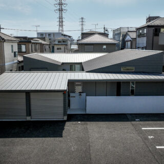 三方を3階建て住宅に囲まれた敷地に建つ平屋。手前は貸し駐車場として使われており、不特定多数の目が届くため、建物は敷地の奥へと配された。