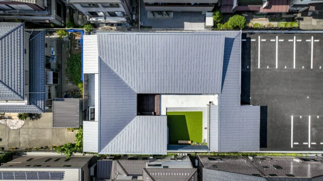 真上から見ると、建物が蛇行しながら中庭を囲んでいるのが分かる。四方を塞がず一箇所を開けることで、風の通り道と外部との接点を残した。屋根は中庭に向かって低くなる片流れに。　