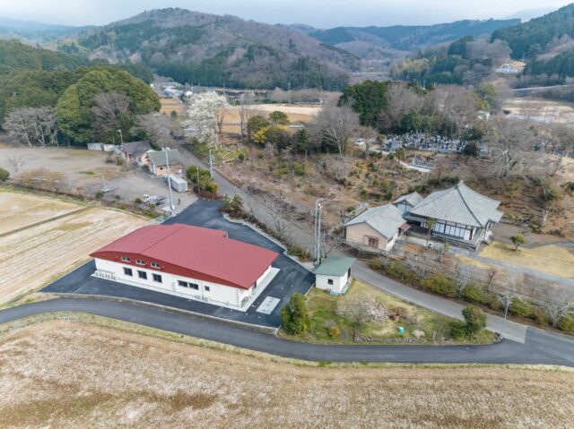 西側からの外観全景。周囲の風景と調和するよう一枚の大きな屋根で覆うデザインを採用した。集会室の高さを確保するためのアシメトリーなフォルムにより、おおらかで心地よいリズムが生まれた